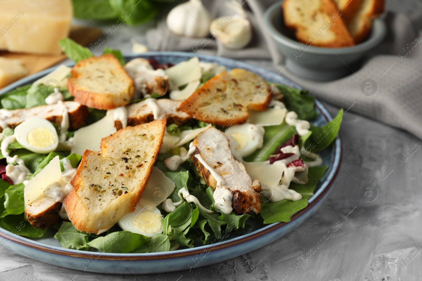 Photo of Tasty Caesar salad with chicken on gray textured table, closeup