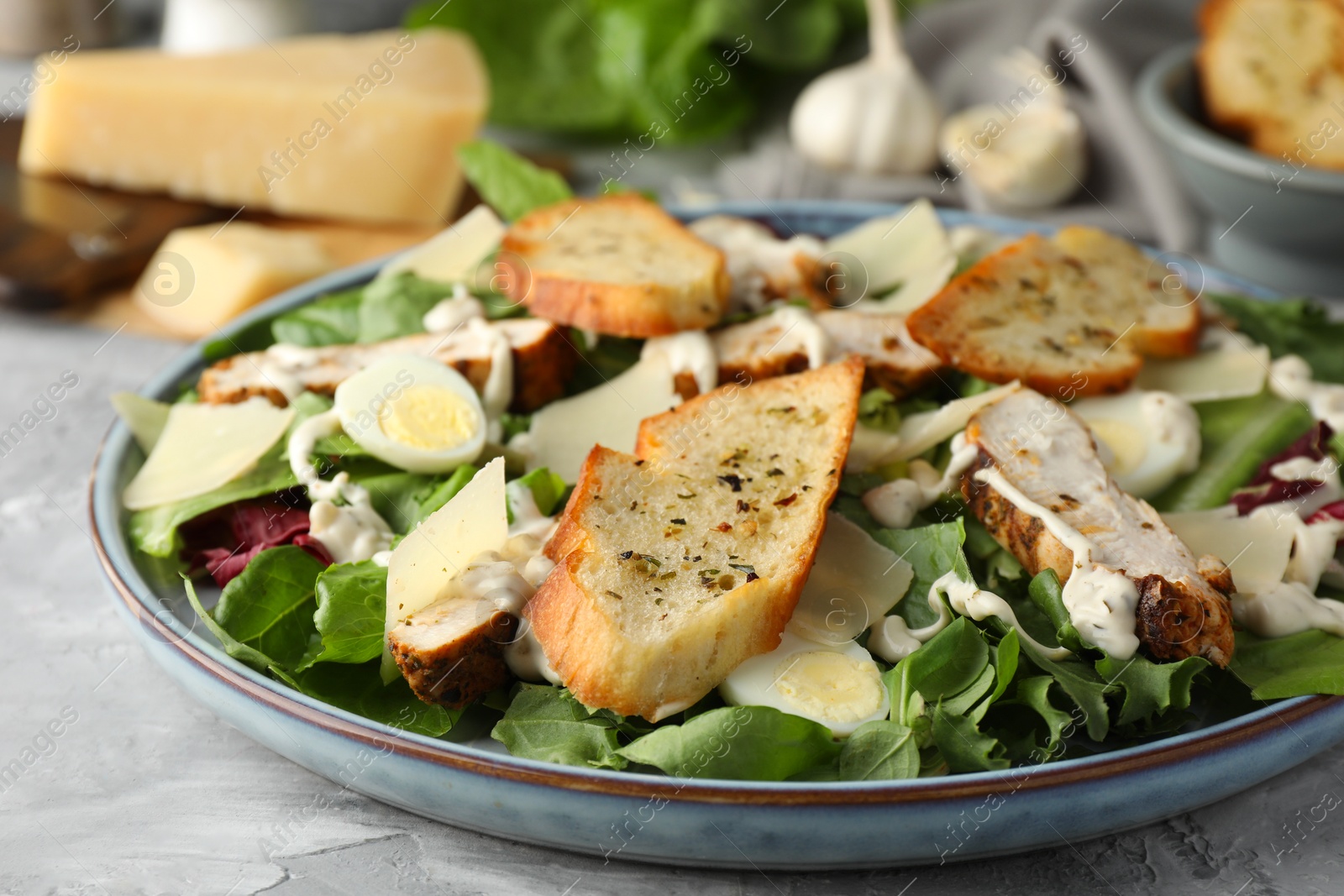 Photo of Tasty Caesar salad with chicken on gray textured table, closeup