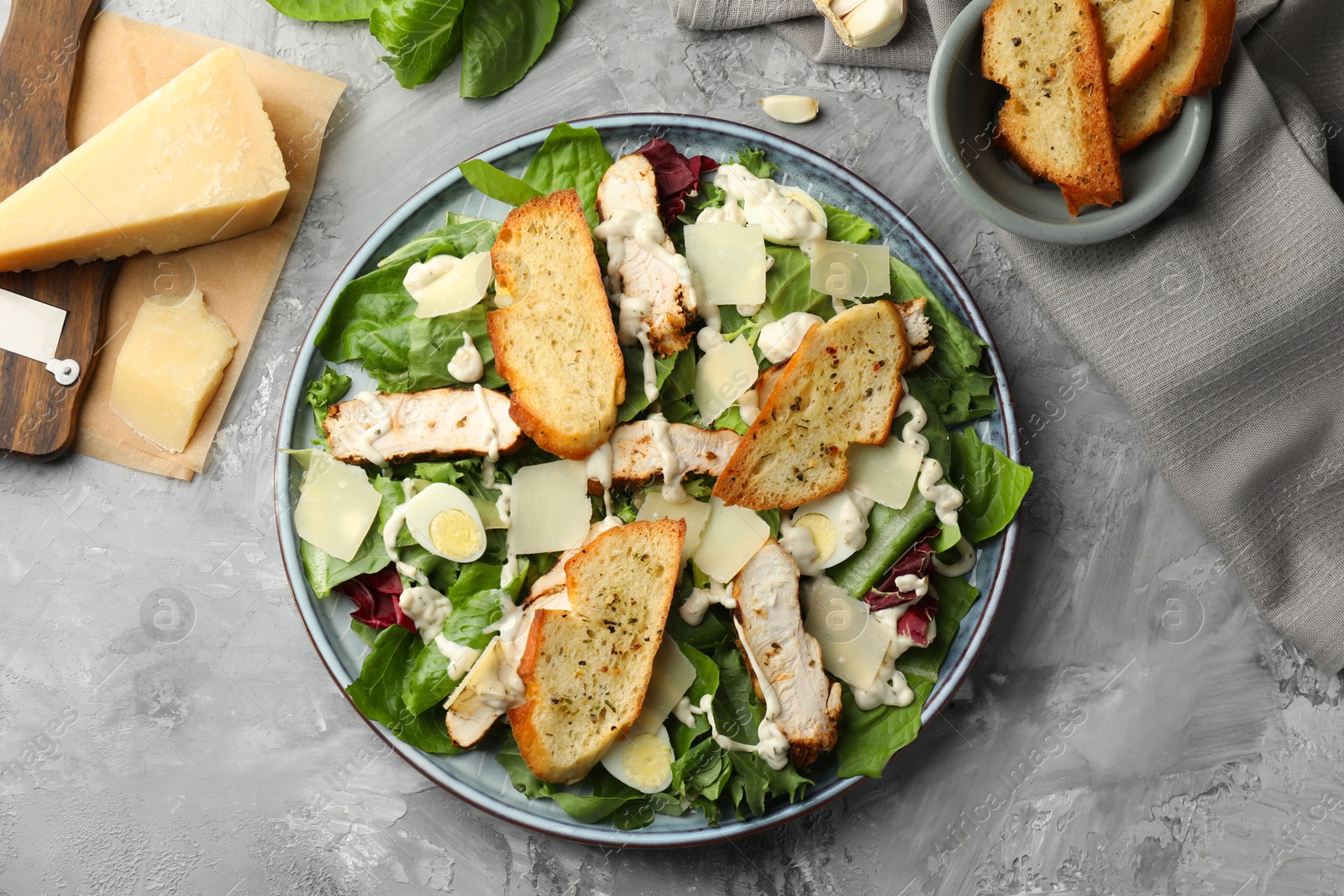 Photo of Tasty Caesar salad with chicken and ingredients on gray textured table, flat lay