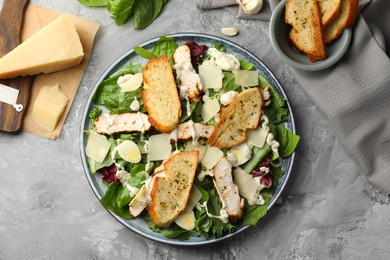 Tasty Caesar salad with chicken and ingredients on gray textured table, flat lay