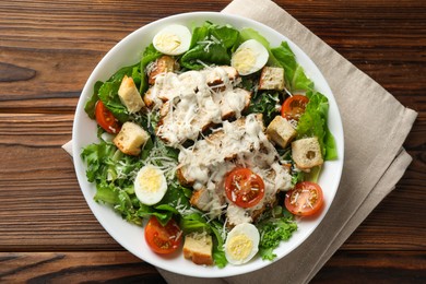 Photo of Tasty Caesar salad with chicken and tomatoes in bowl on wooden table, top view