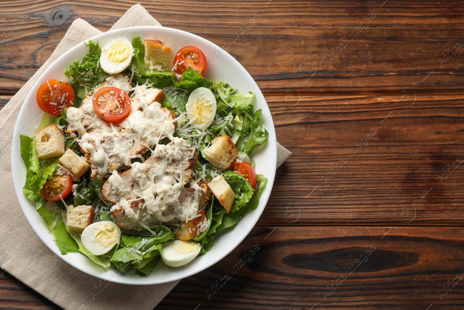 Photo of Tasty Caesar salad with chicken and tomatoes in bowl on wooden table, top view. Space for text