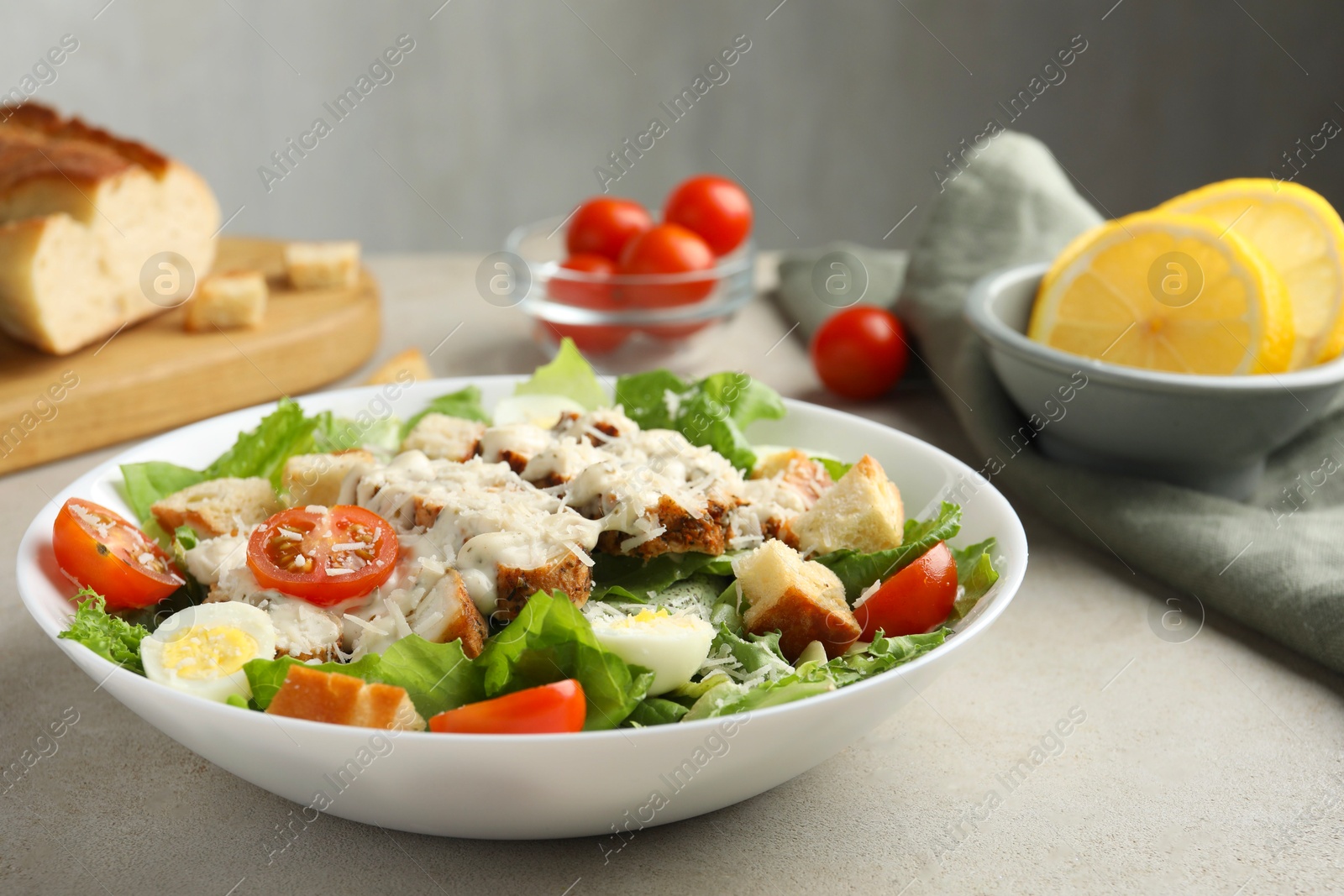 Photo of Tasty Caesar salad with chicken and tomatoes in bowl on gray textured table