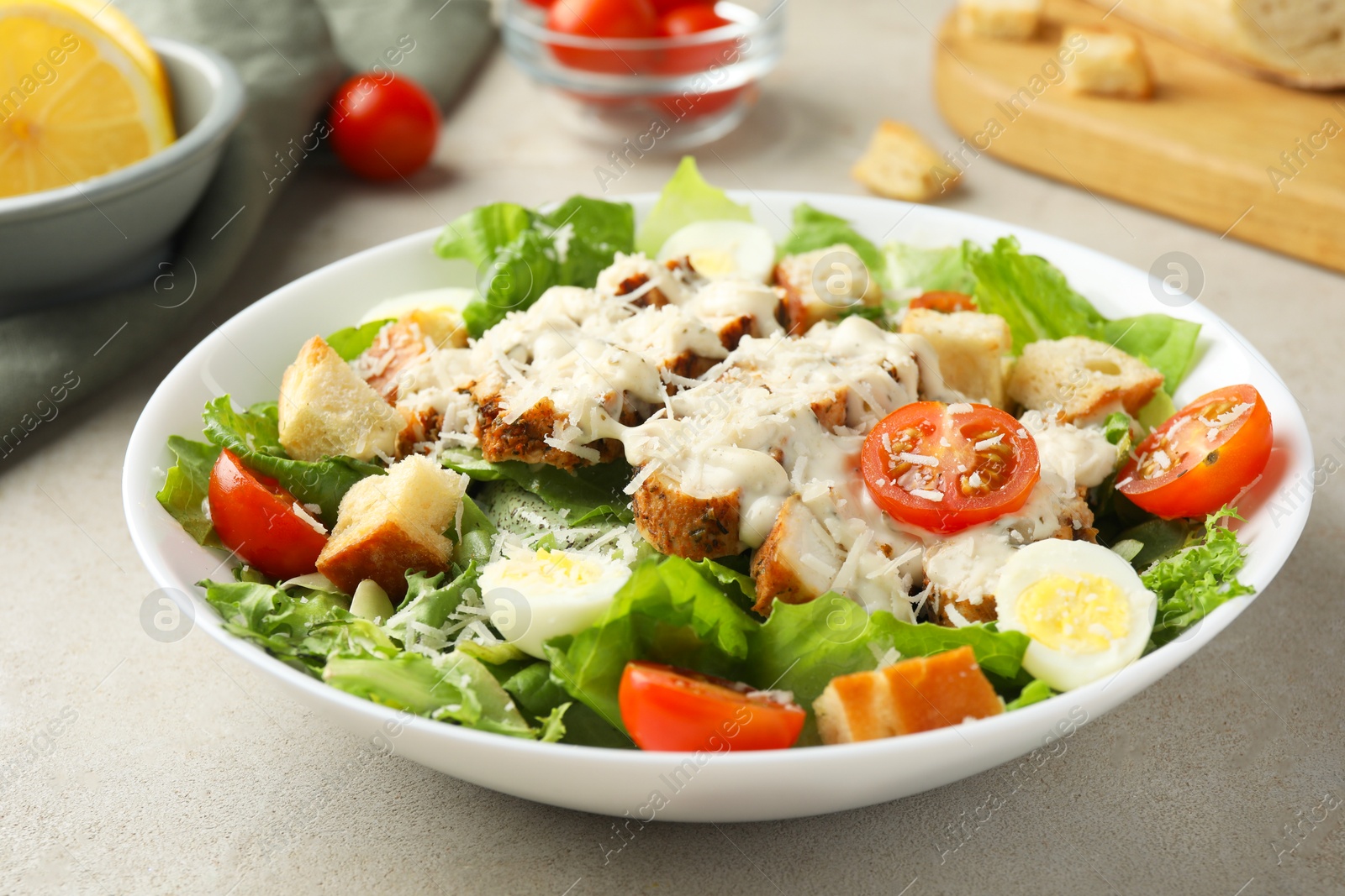 Photo of Tasty Caesar salad with chicken and tomatoes in bowl on gray textured table, closeup