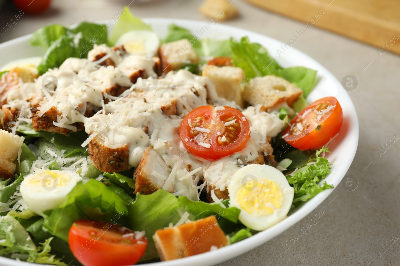 Photo of Tasty Caesar salad with chicken and tomatoes in bowl on gray textured table, closeup