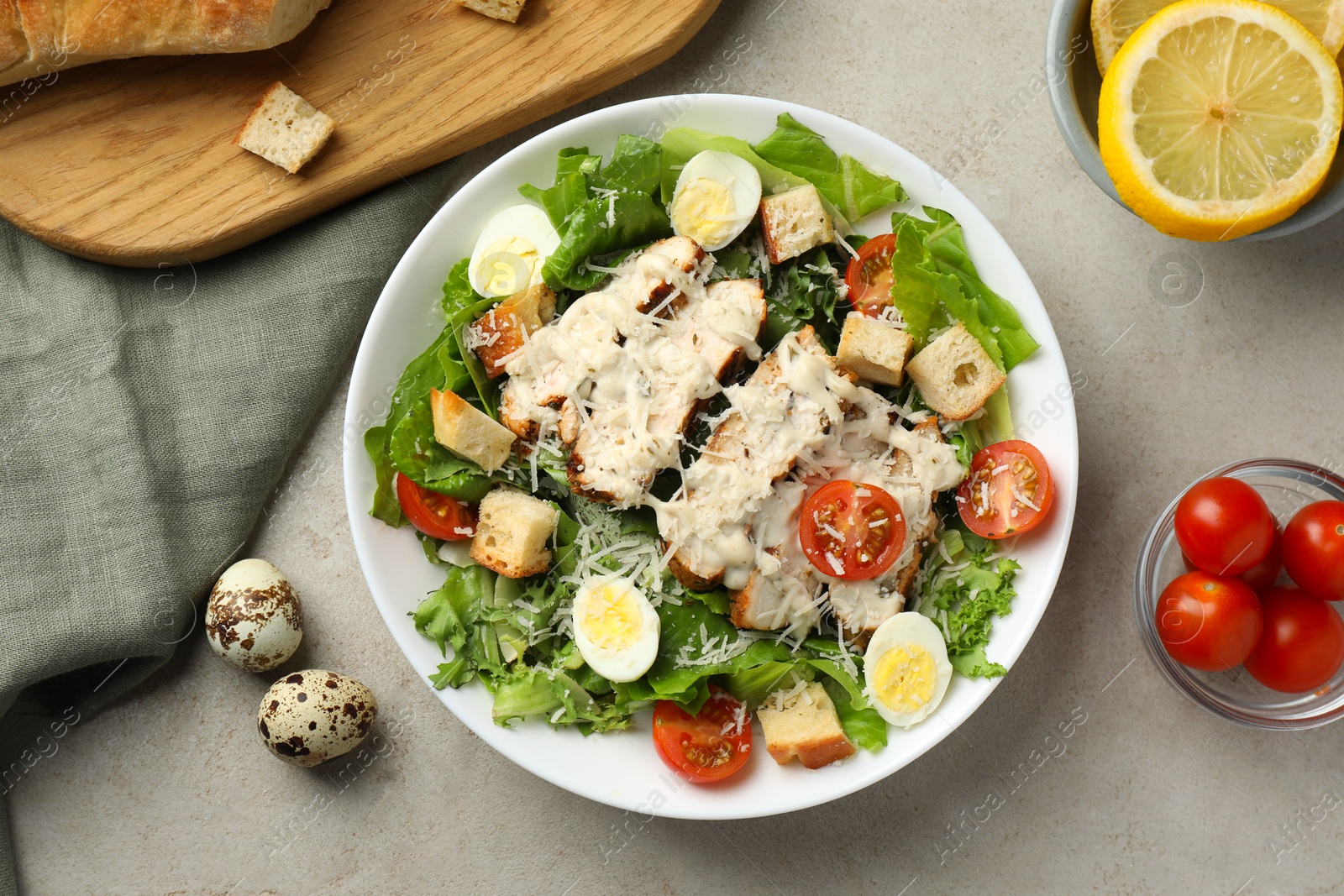 Photo of Tasty Caesar salad with chicken and tomatoes in bowl on gray textured table, flat lay