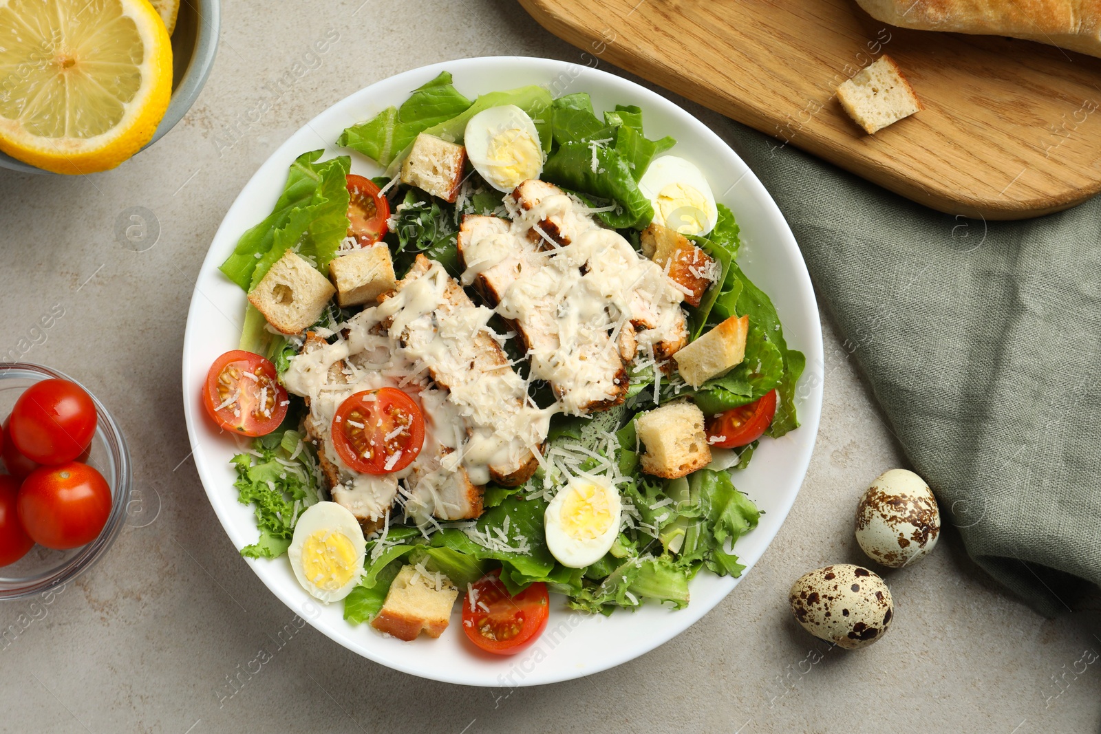 Photo of Tasty Caesar salad with chicken and tomatoes in bowl on gray textured table, flat lay