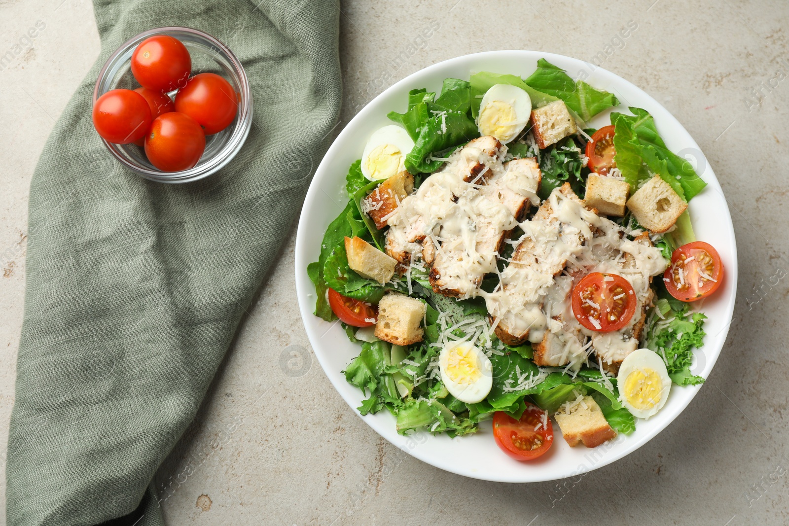 Photo of Tasty Caesar salad with chicken and tomatoes in bowl on gray textured table, flat lay