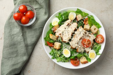 Photo of Tasty Caesar salad with chicken and tomatoes in bowl on gray textured table, flat lay