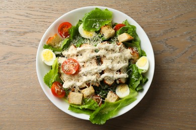 Tasty Caesar salad with chicken and tomatoes in bowl on wooden table, top view