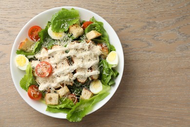 Photo of Tasty Caesar salad with chicken and tomatoes in bowl on wooden table, top view. Space for text