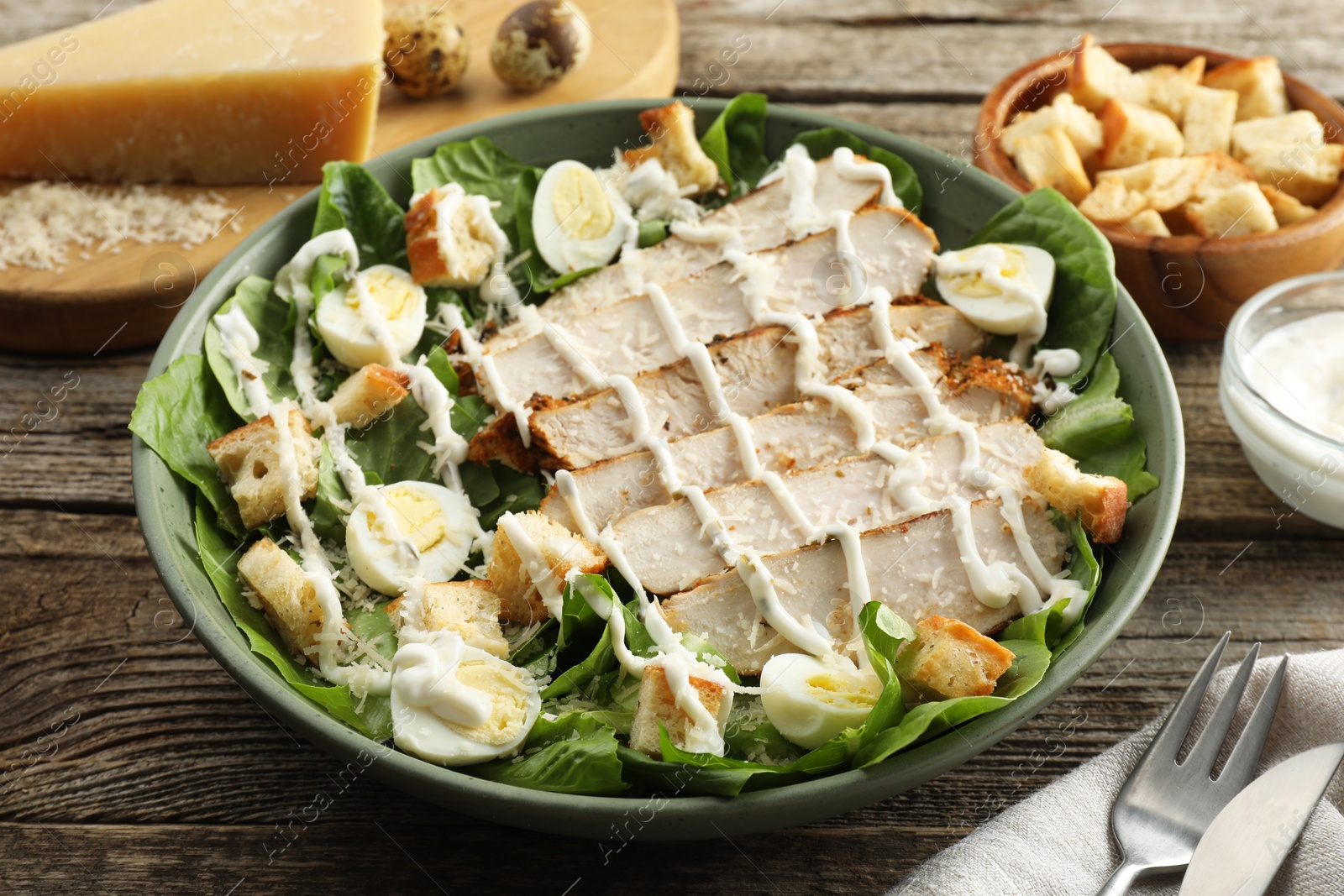 Photo of Delicious Caesar salad with chicken on wooden table, closeup