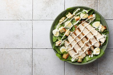 Photo of Delicious Caesar salad with chicken on textured tiled table, top view. Space for text