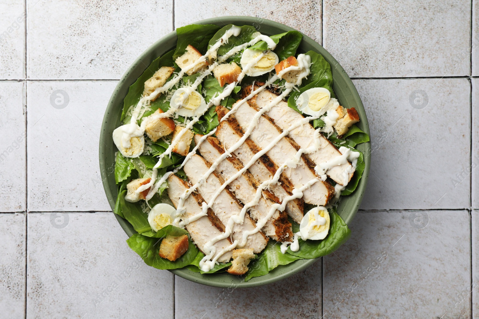 Photo of Delicious Caesar salad with chicken on textured tiled table, top view