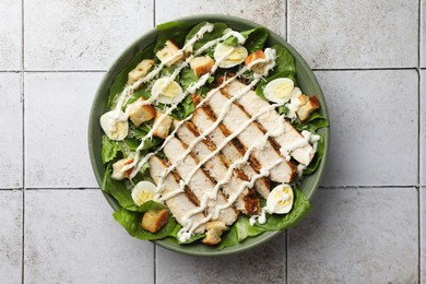 Delicious Caesar salad with chicken on textured tiled table, top view