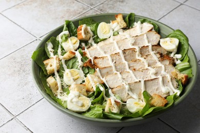 Photo of Delicious Caesar salad with chicken on textured tiled table, closeup