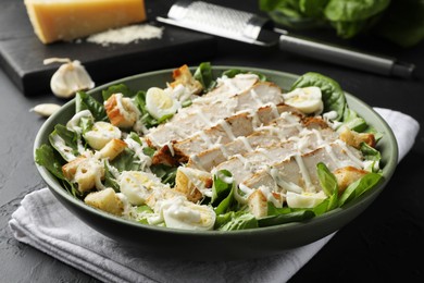 Photo of Delicious Caesar salad with chicken on black textured table, closeup