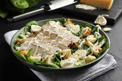 Photo of Delicious Caesar salad with chicken on black textured table, closeup