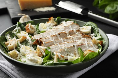 Photo of Delicious Caesar salad with chicken on black textured table, closeup