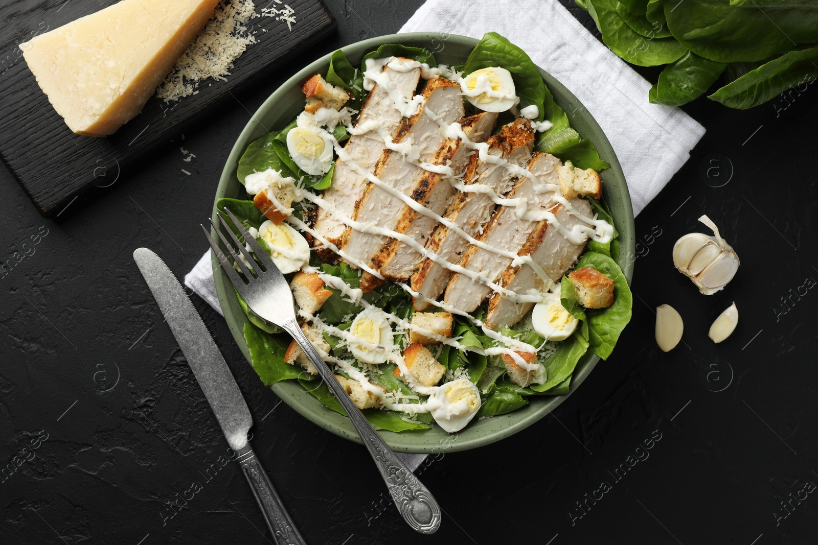 Photo of Delicious Caesar salad with chicken on black textured table, flat lay