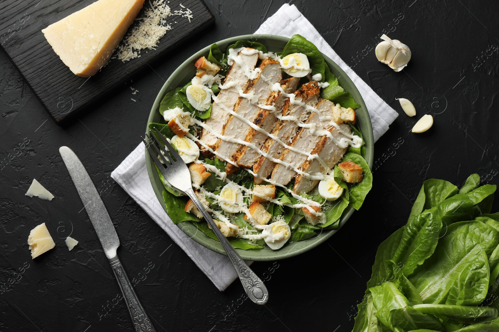 Photo of Delicious Caesar salad with chicken on black textured table, flat lay