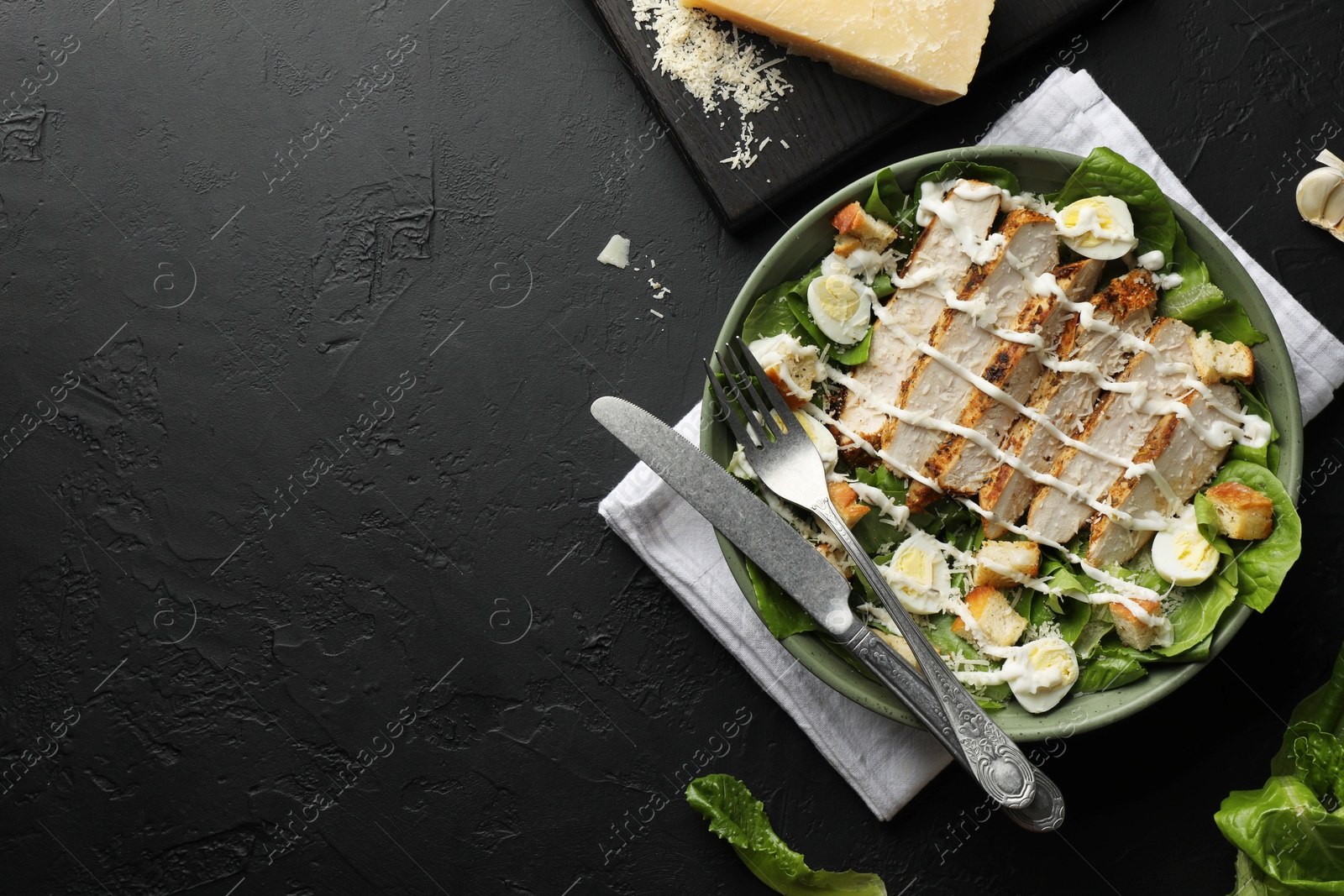 Photo of Delicious Caesar salad with chicken on black textured table, flat lay. Space for text