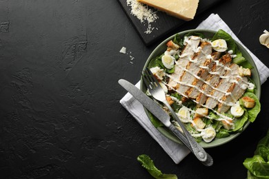 Photo of Delicious Caesar salad with chicken on black textured table, flat lay. Space for text