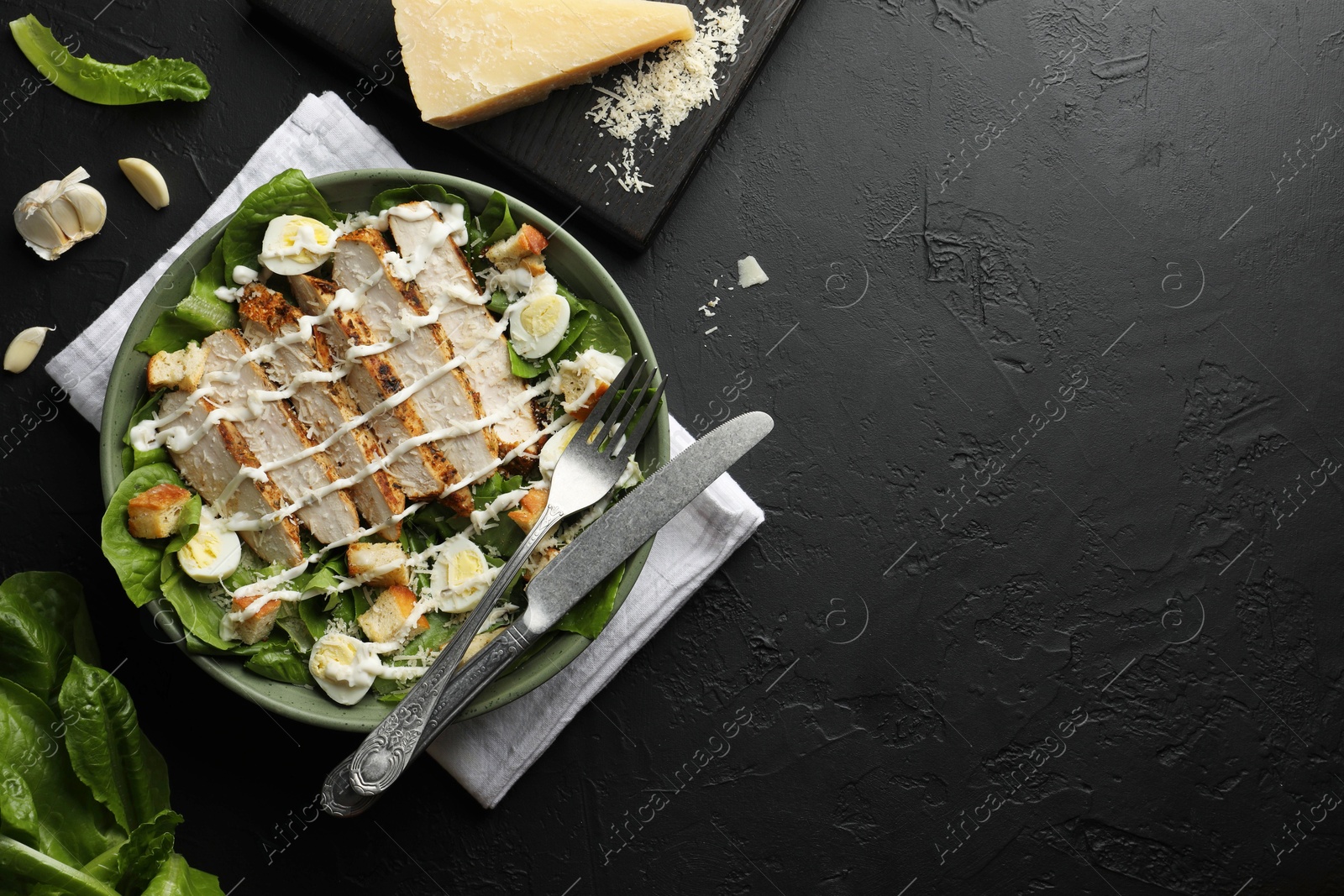 Photo of Delicious Caesar salad with chicken on black textured table, flat lay. Space for text