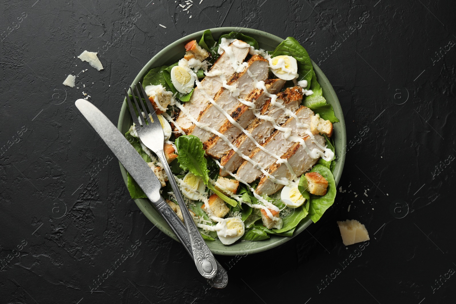 Photo of Delicious Caesar salad with chicken on black textured table, top view