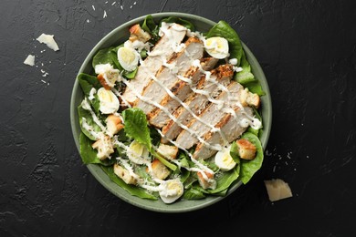 Photo of Delicious Caesar salad with chicken on black textured table, top view