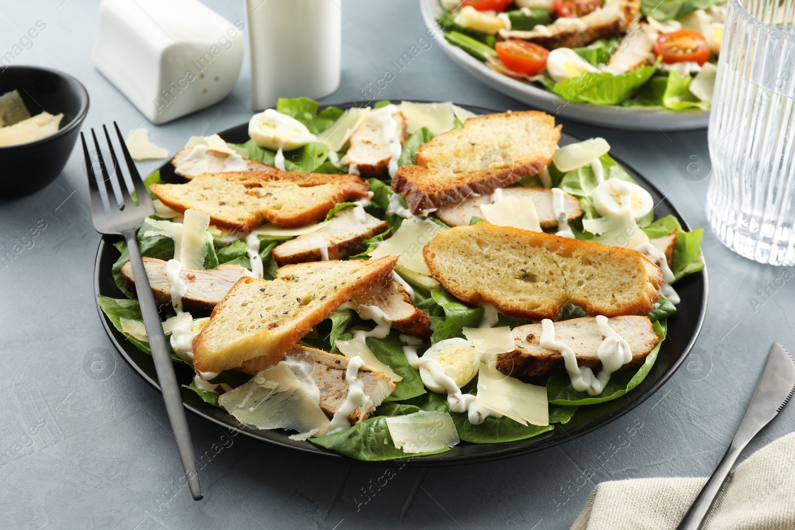 Photo of Delicious Caesar salad with chicken on grey textured table