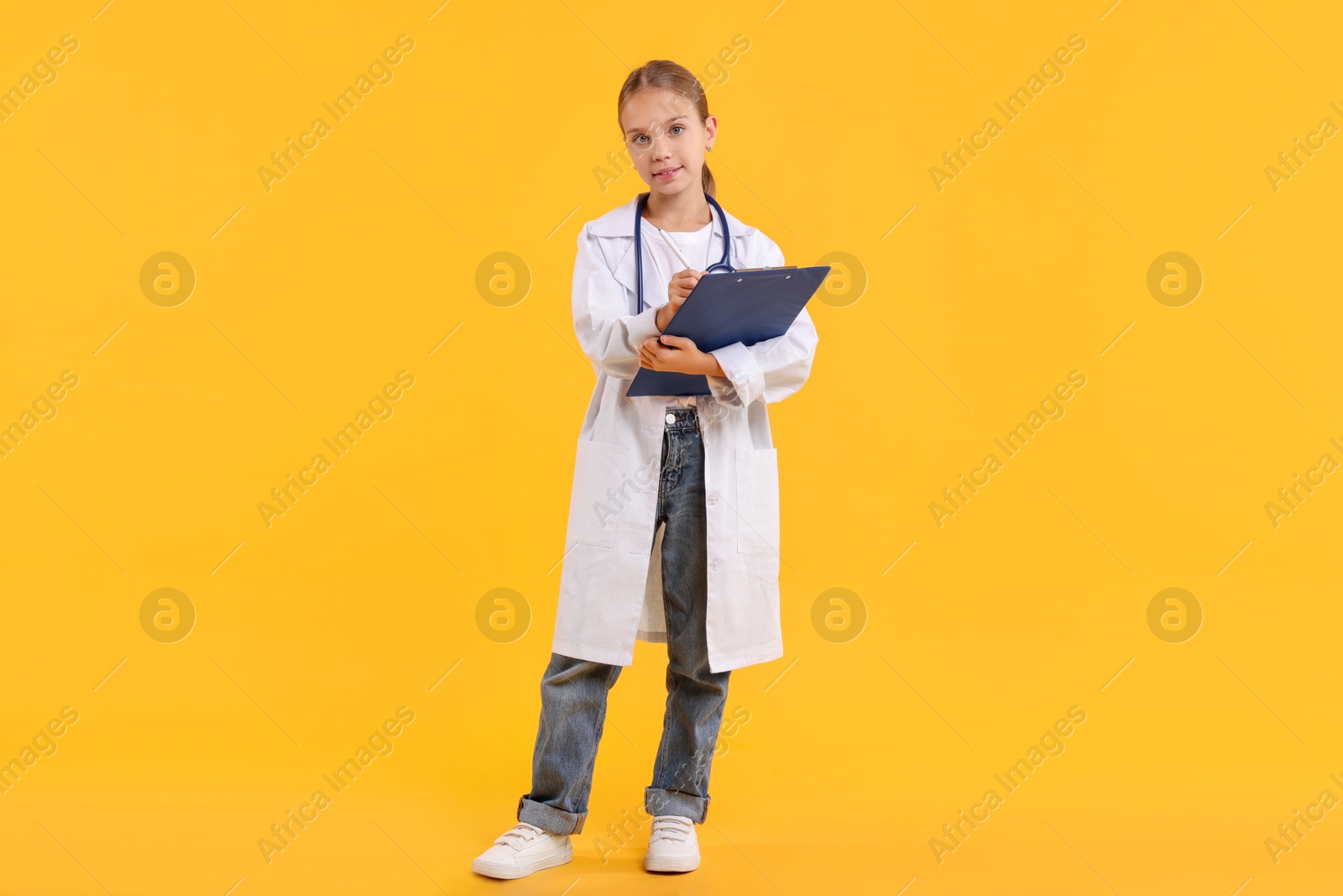 Photo of Girl with stethoscope and clipboard pretending to be doctor on yellow background. Dreaming of future profession