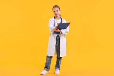 Photo of Girl with stethoscope and clipboard pretending to be doctor on yellow background. Dreaming of future profession