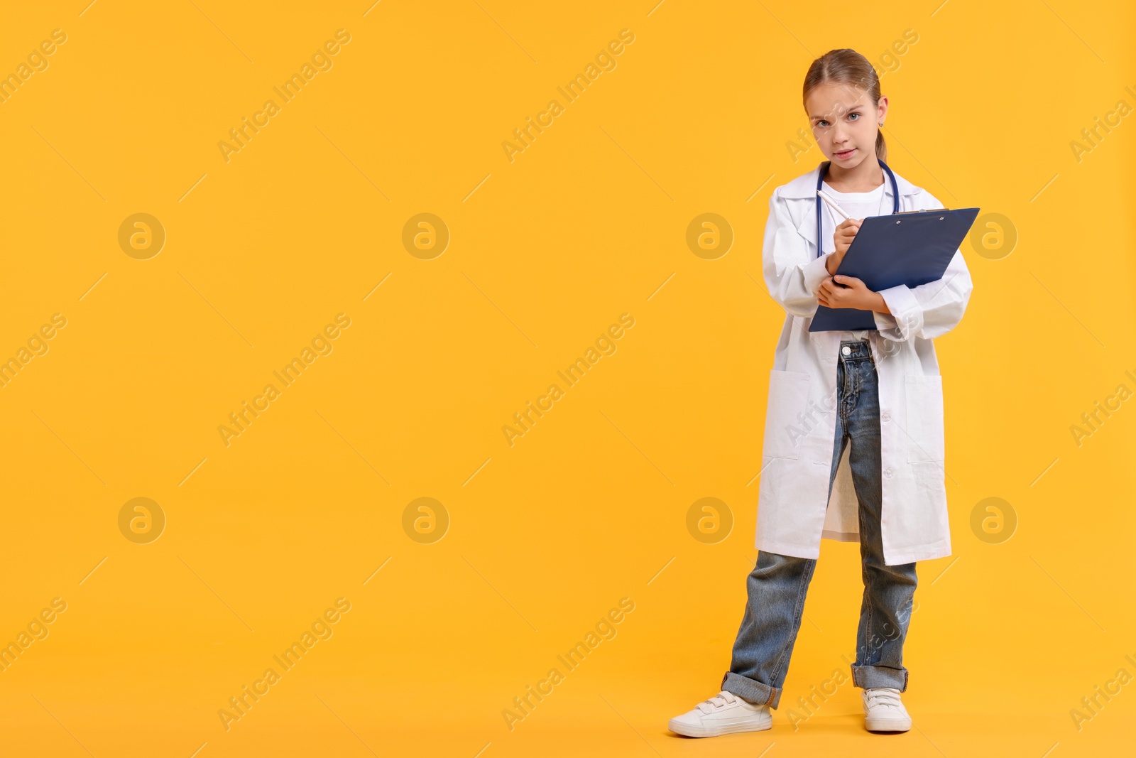 Photo of Girl with stethoscope and clipboard pretending to be doctor on yellow background, space for text. Dreaming of future profession