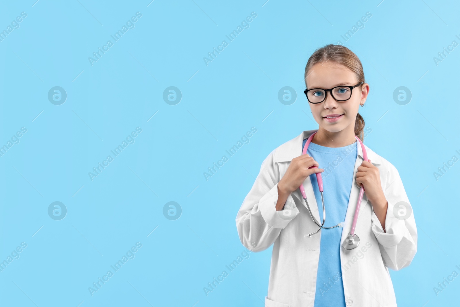 Photo of Girl with stethoscope pretending to be doctor on light blue background, space for text. Dreaming of future profession