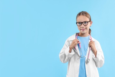 Photo of Girl with stethoscope pretending to be doctor on light blue background, space for text. Dreaming of future profession