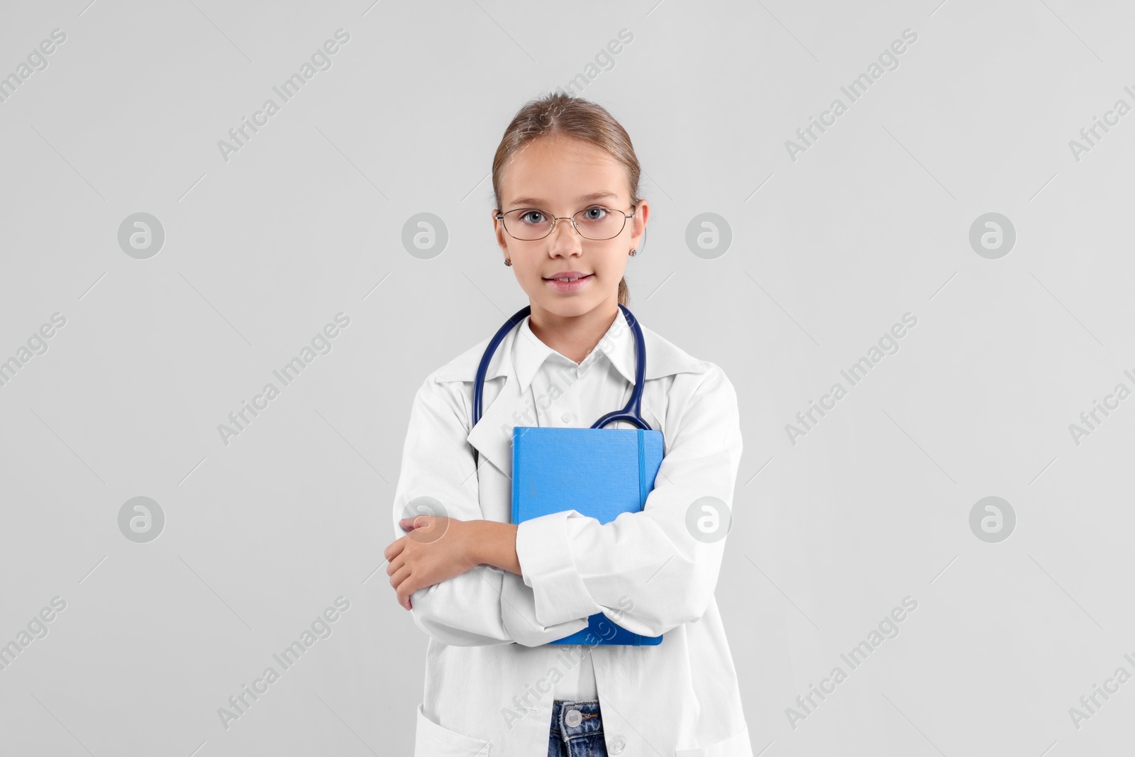 Photo of Girl with stethoscope and book pretending to be doctor on light grey background. Dreaming of future profession