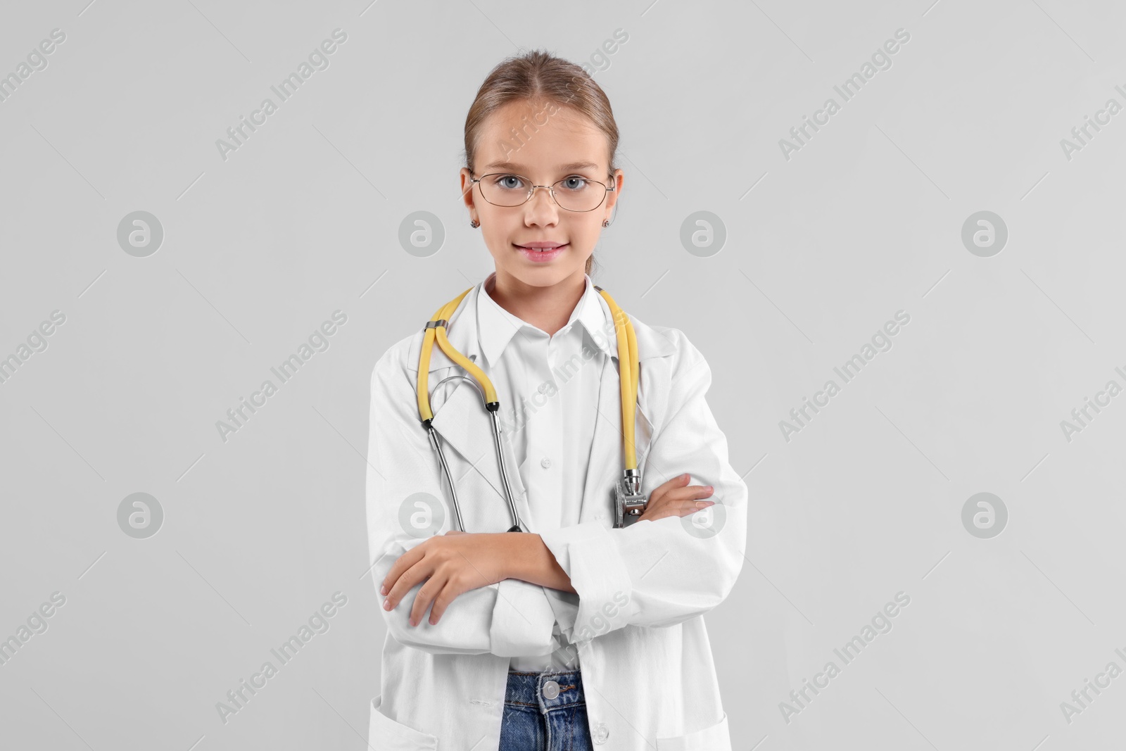 Photo of Girl with stethoscope pretending to be doctor on light grey background. Dreaming of future profession