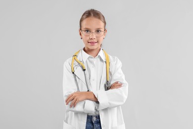 Photo of Girl with stethoscope pretending to be doctor on light grey background. Dreaming of future profession