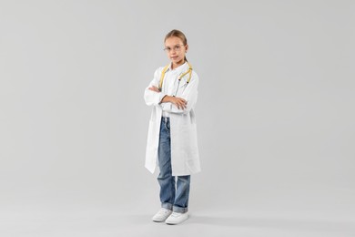 Photo of Girl with stethoscope pretending to be doctor on light grey background. Dreaming of future profession