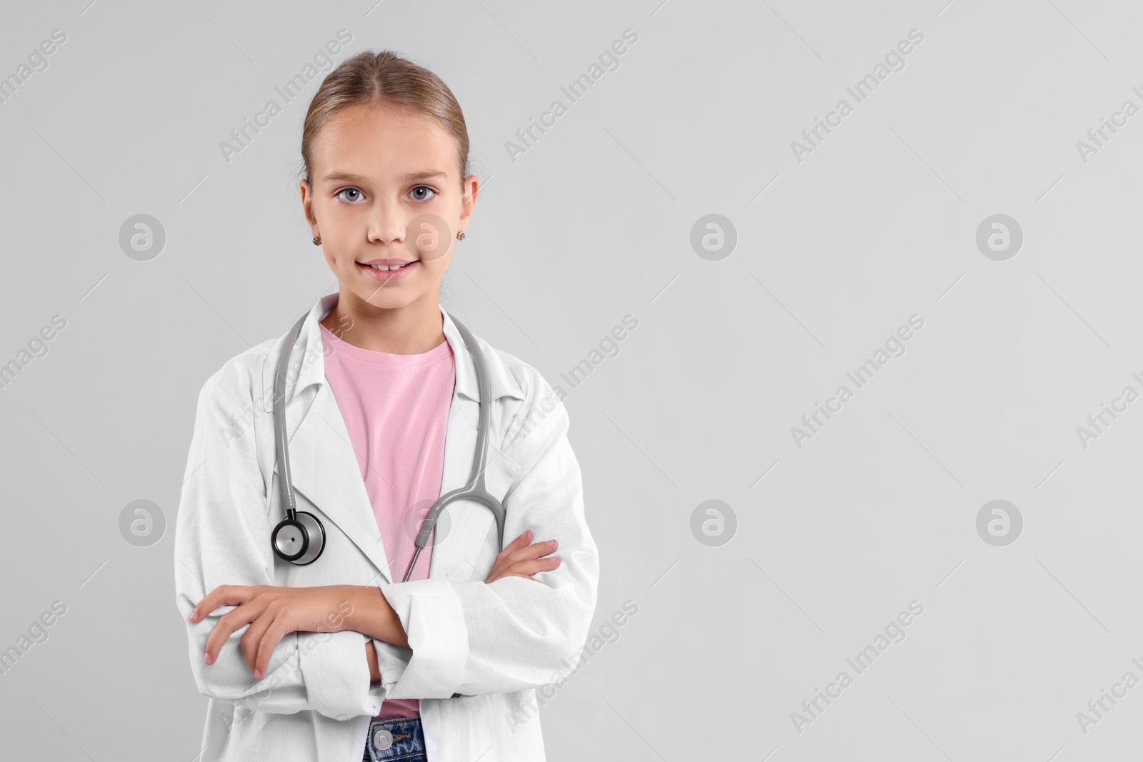 Photo of Girl with stethoscope pretending to be doctor on light grey background, space for text. Dreaming of future profession