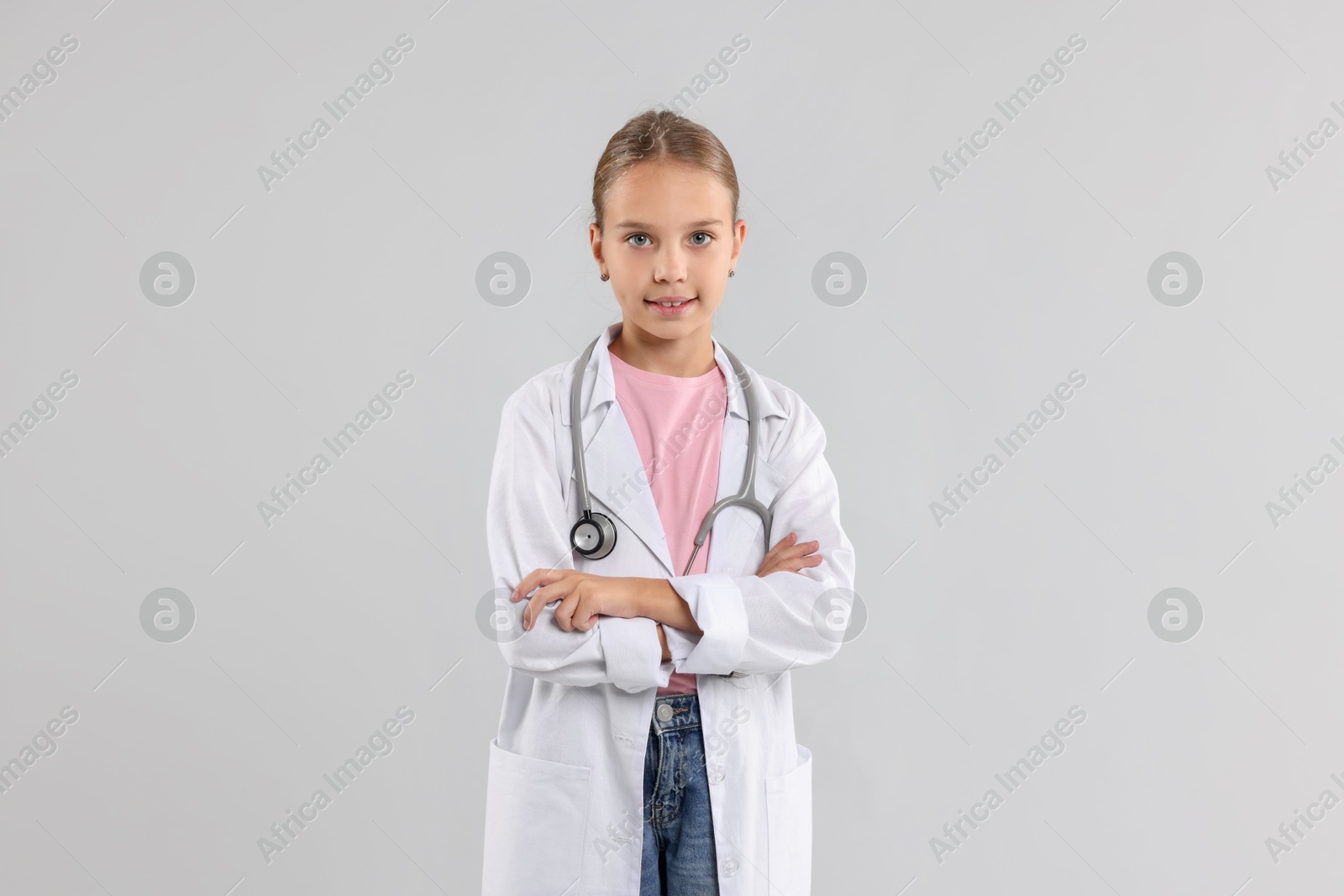 Photo of Girl with stethoscope pretending to be doctor on light grey background. Dreaming of future profession