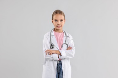 Photo of Girl with stethoscope pretending to be doctor on light grey background. Dreaming of future profession