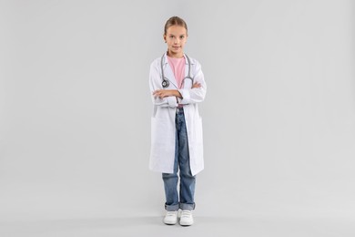 Photo of Girl with stethoscope pretending to be doctor on light grey background. Dreaming of future profession