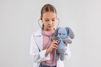 Photo of Girl with stethoscope and toy pretending to be doctor on light grey background. Dreaming of future profession