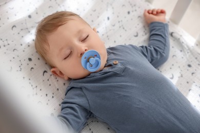 Cute baby with pacifier sleeping in crib at home