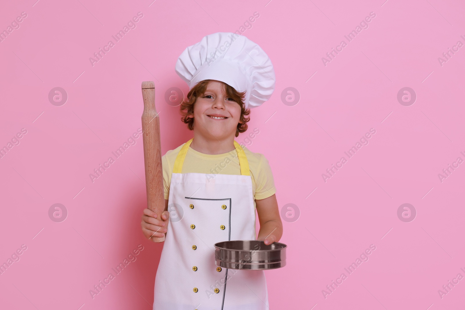 Photo of Little boy with utensils pretending to be chef on pink background. Dreaming about future profession