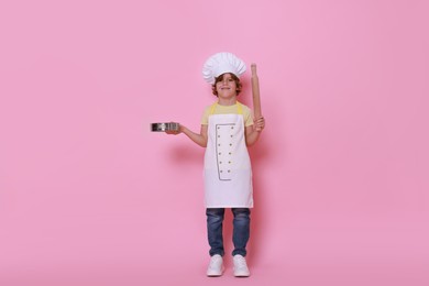 Photo of Little boy with utensils pretending to be chef on pink background. Dreaming about future profession