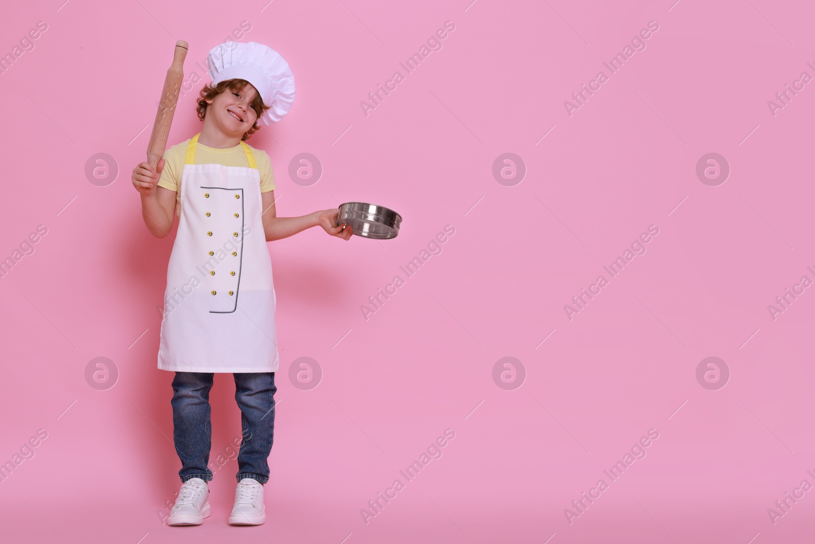 Photo of Little boy with utensils pretending to be chef on pink background, space for text. Dreaming about future profession