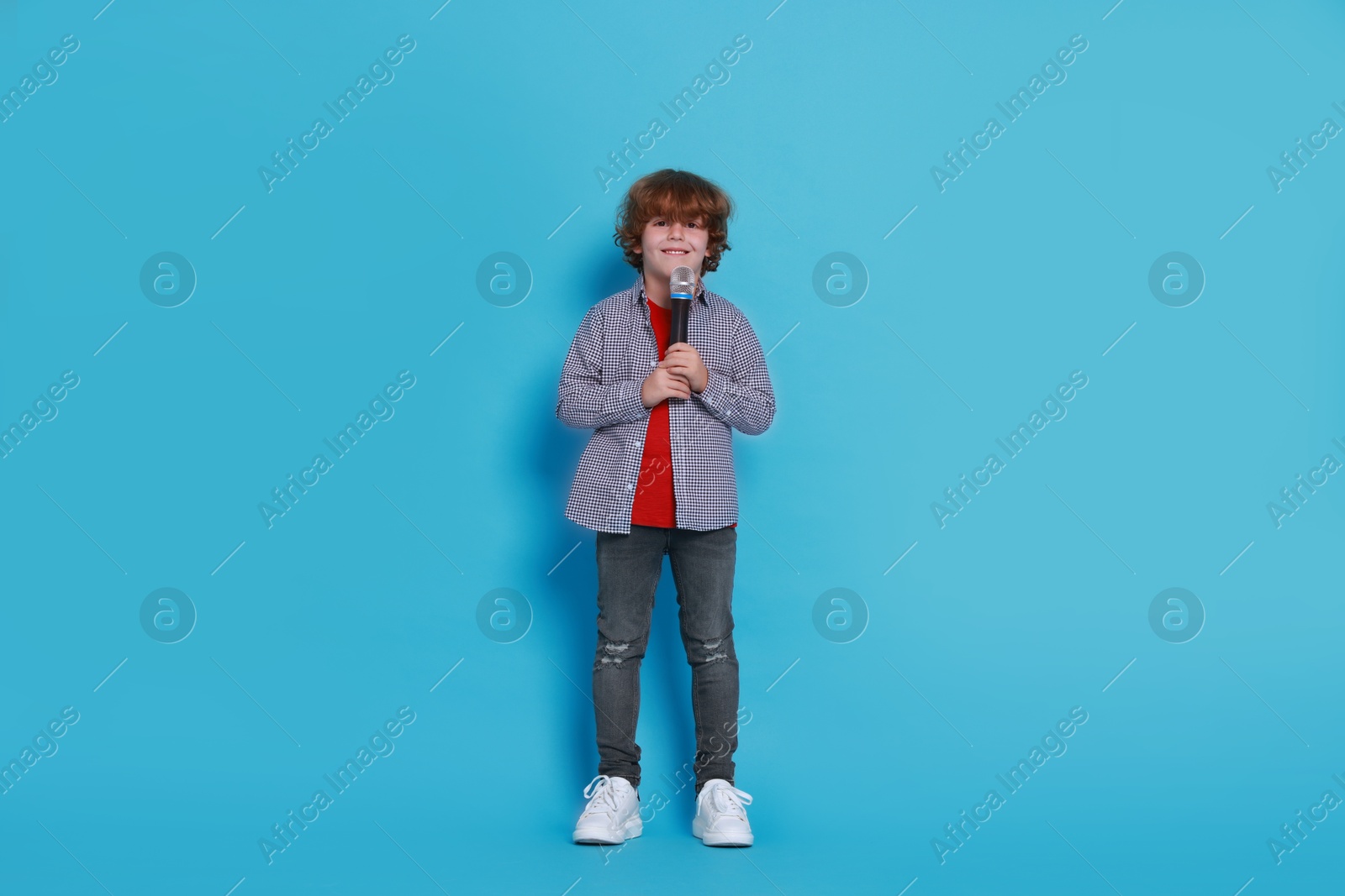 Photo of Little boy with microphone pretending to be singer on light blue background. Dreaming about future profession